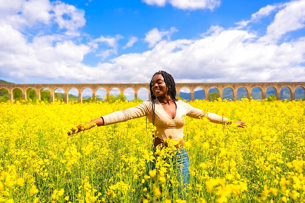 Lifestyle, enjoying nature in freedom, portrait of a black ethnic girl with braids, in a field of yellow flowers