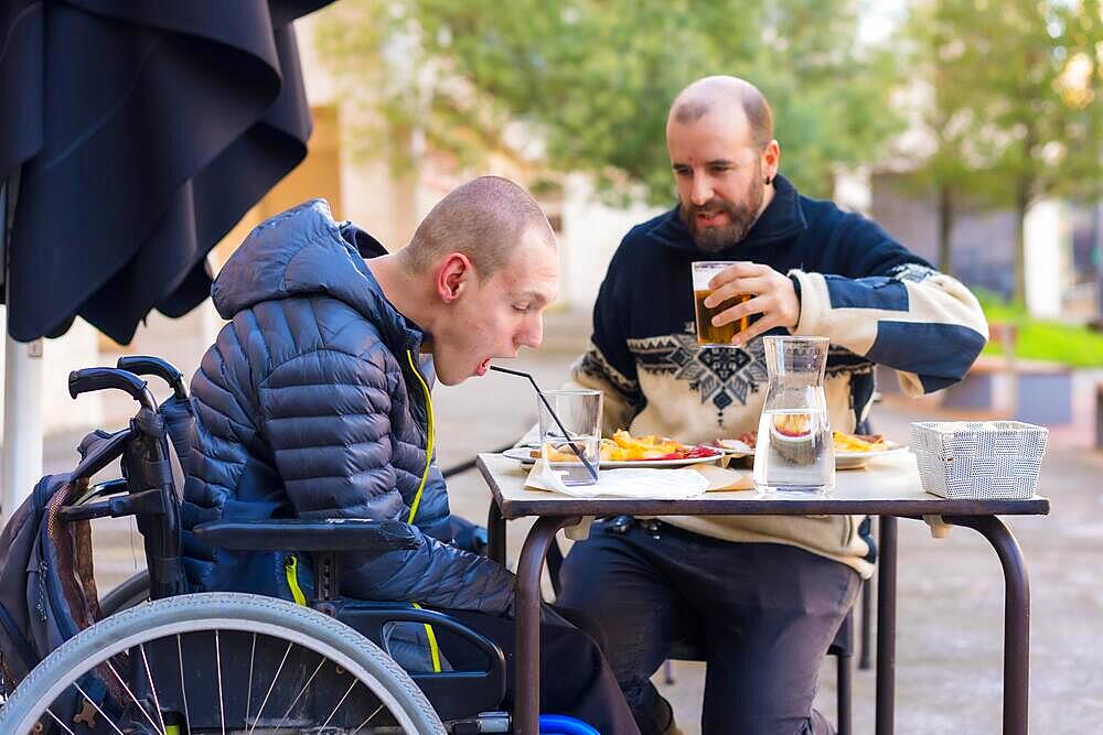 A disabled person eating on the terrace of a restaurant with a friend having fun