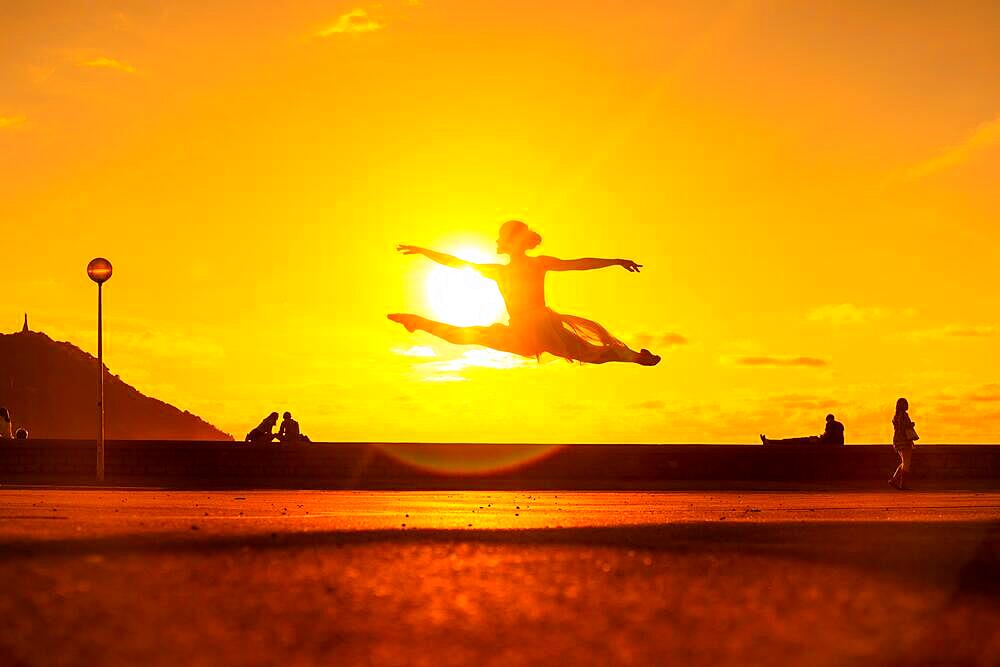 Silhouette of a young female dancer performing a jump along the beach at sunset