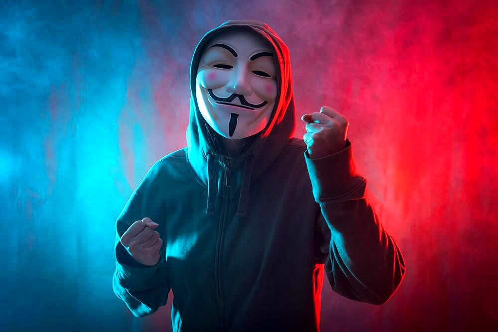 Hacker with anonymous mask with a symbol of fight, with a background of smoke and colored led