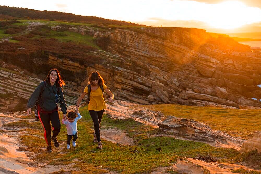 Two sisters with a child watching the sunset on the coast by the sea, family lifestyle