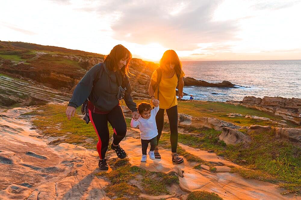 Lgbt couple of women with a child at sunset on the coast by the sea, family lifestyle