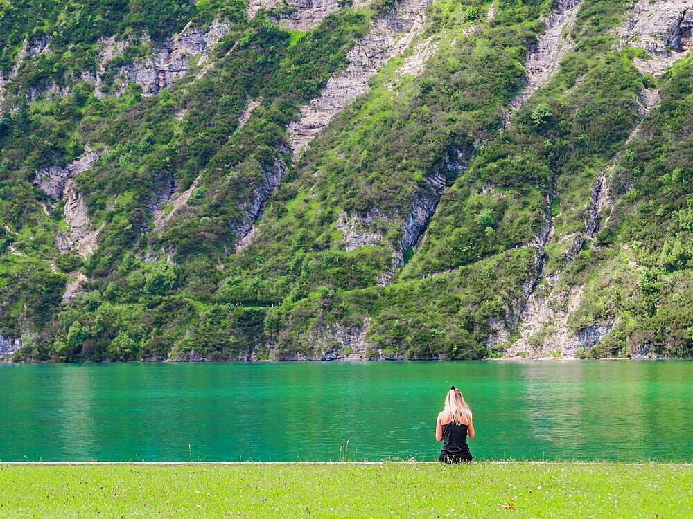 Young girl sitting at the shore of Achensee, Austria in front of impressing cliff