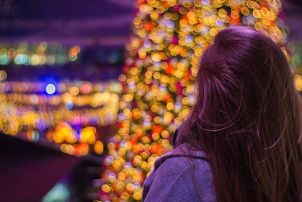 Girl in front of a blurred view of Christmas tree with fairy lights