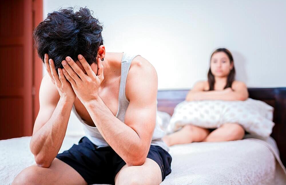 Worried man sitting on the side of the bed and angry wife. Worried man in bed with erectile dysfunction. Concept of crisis and couple problems in bed, Managua, Nicaragua, Central America