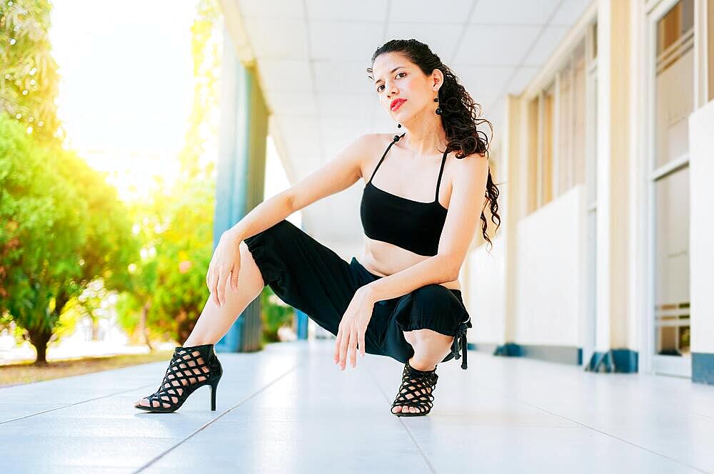 Portrait of dancer Woman in heels on the floor looking at the camera. Portrait of dance girl in high heels crouching on the floor, Dance artist woman in high heels outdoors