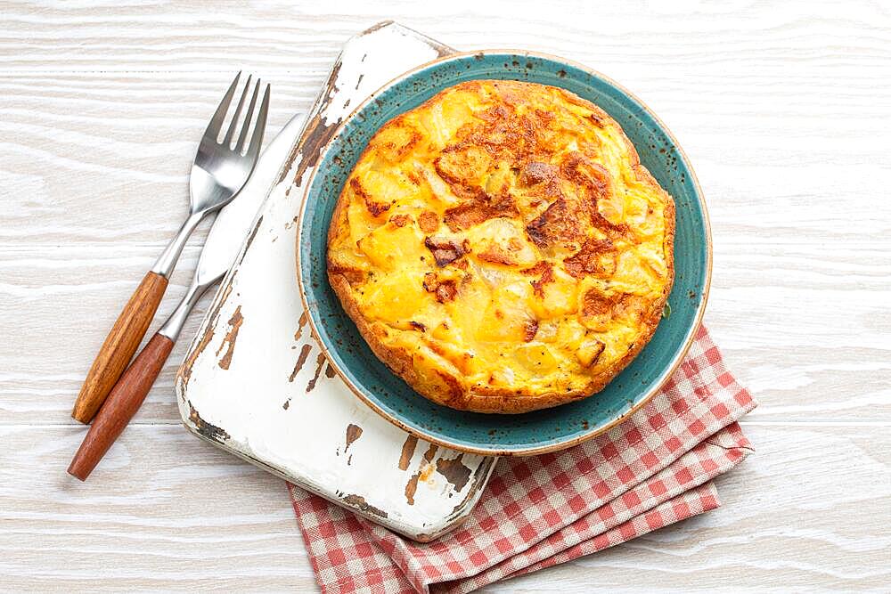 Homemade Spanish tortilla - omelette with potatoes on plate on white wooden rustic background top view. Traditional dish of Spain Tortilla de patatas for lunch or snack, overhead