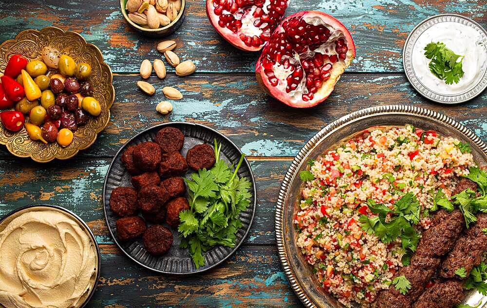 Various Turkish dishes: meat kebab with tabbouleh salad, falafel, hummus, olives, pistachios and other Middle Eastern meze on wooden table top view. Ethnic arab food, cuisine of Turkey