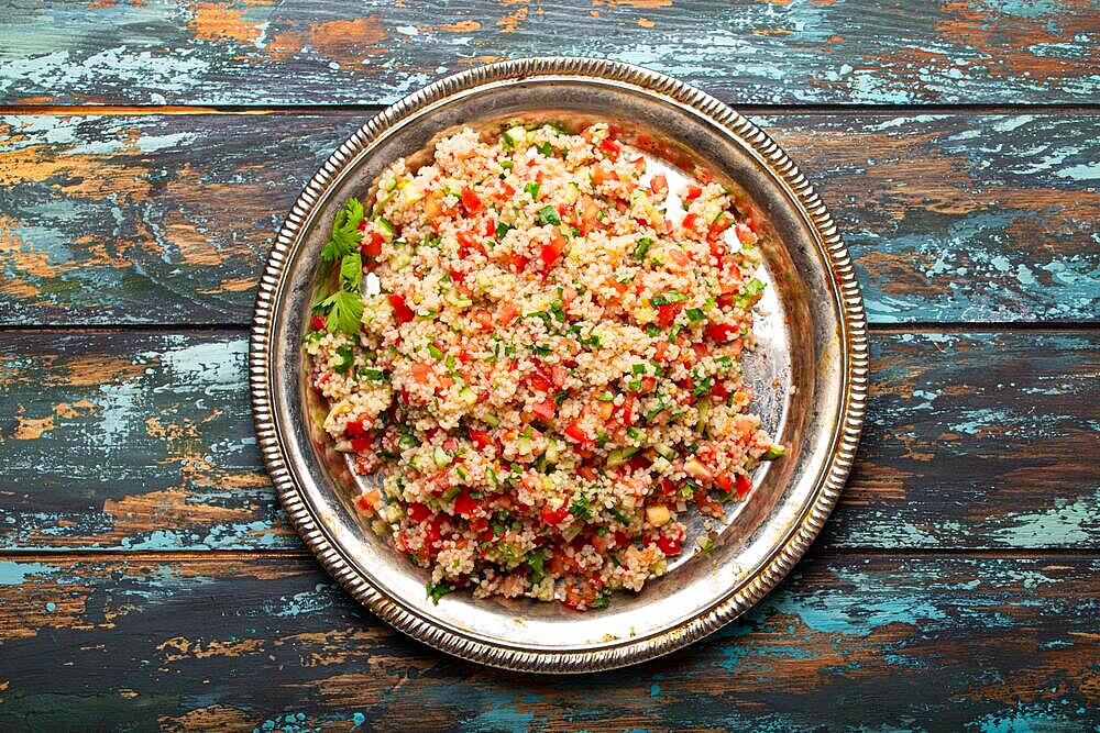 Middle eastern and Mediterranean traditional vegetable salad tabbouleh with couscous on rustic metal plate and wooden background from above. Arab Turkish food