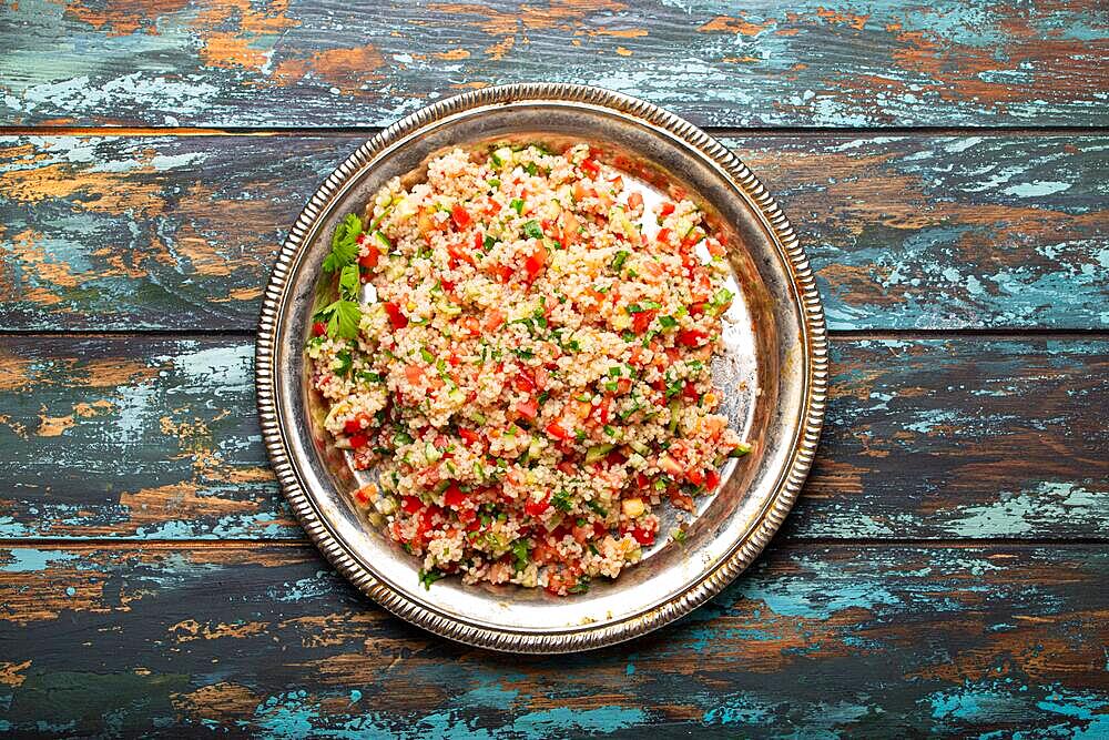 Middle eastern and Mediterranean traditional vegetable salad tabbouleh with couscous on rustic metal plate and wooden background from above. Arab Turkish food