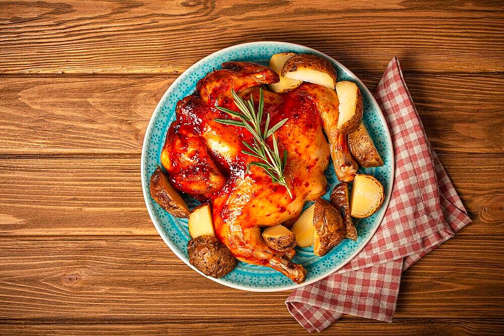 Delicious roasted whole chicken with glazed gold crispy skin on big ceramic plate top view on wooden rustic background top view, traditional tasty dinner