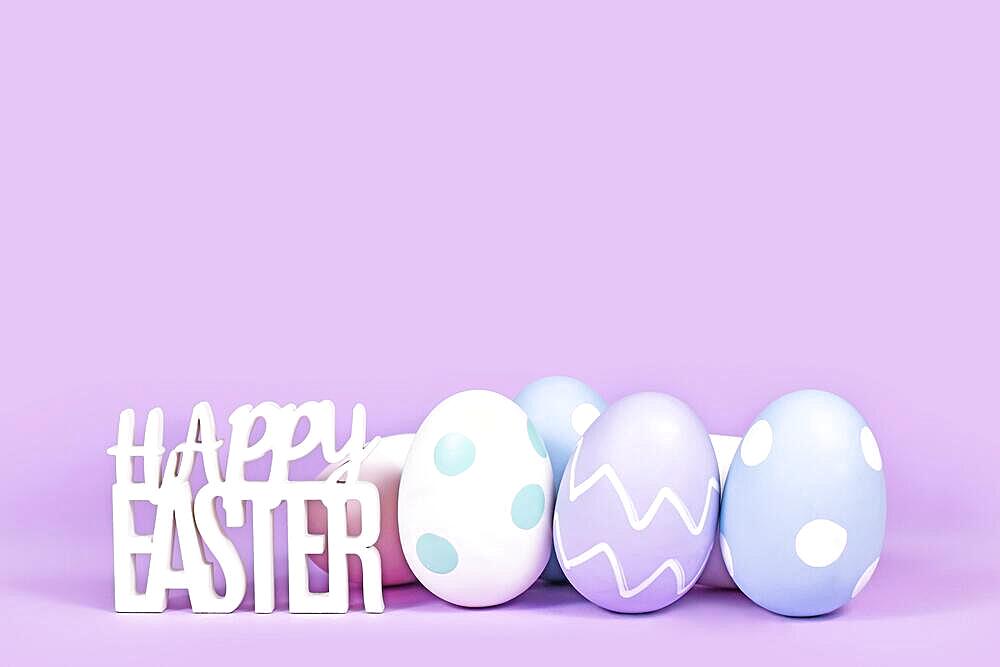 Pastel colored easter eggs and text Happy Easter on violet background with copy space