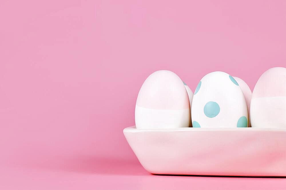 Pastel colored painted Easter eggs in egg box on pink background with copy space