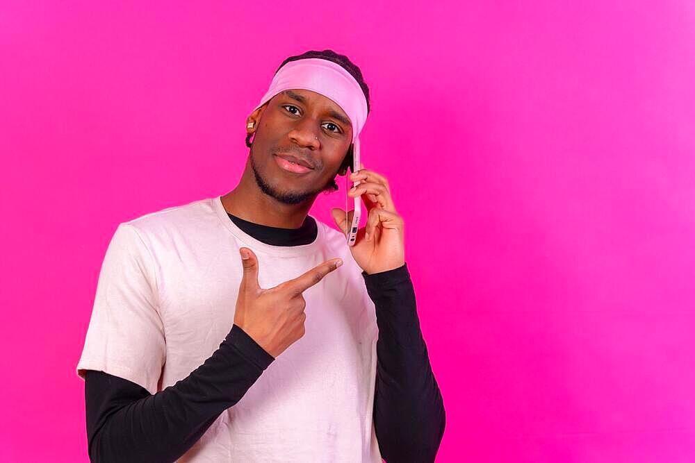 Black ethnic man with a phone in pink clothes on a pink background, pointing at the phone