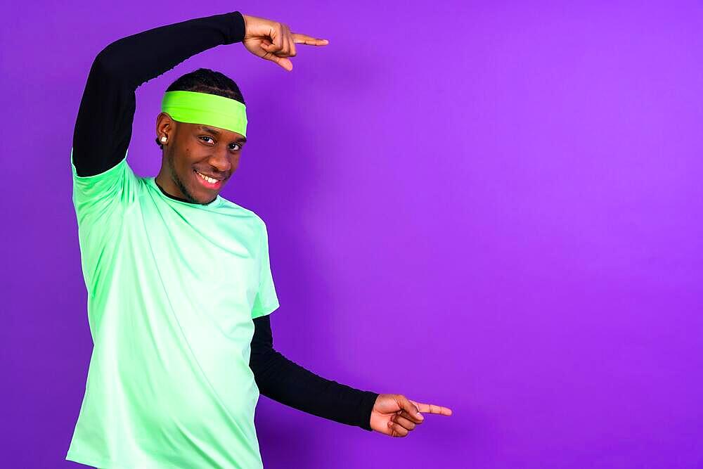 Black ethnic man in green clothes on a purple background, pointing to a free right copy space