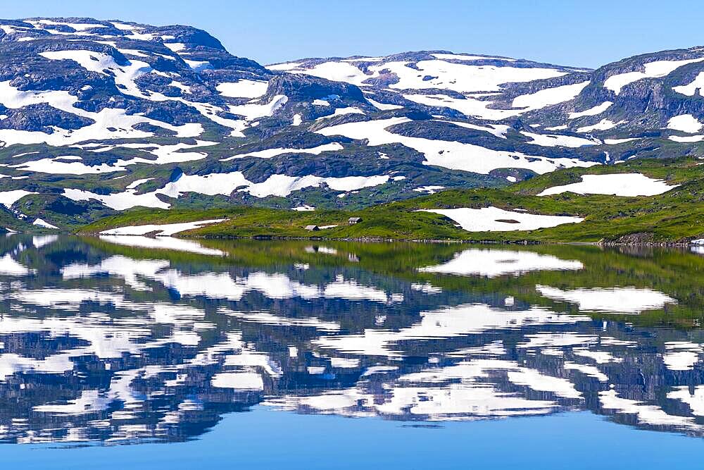 Reflection of partly snow-covered mountains in Lake Stavatn in Haukelifjell, Hardangervidda, Norway, Europe