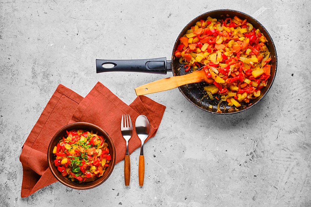 Top view of rustic vegetable ragout in clay bowl and frying pan