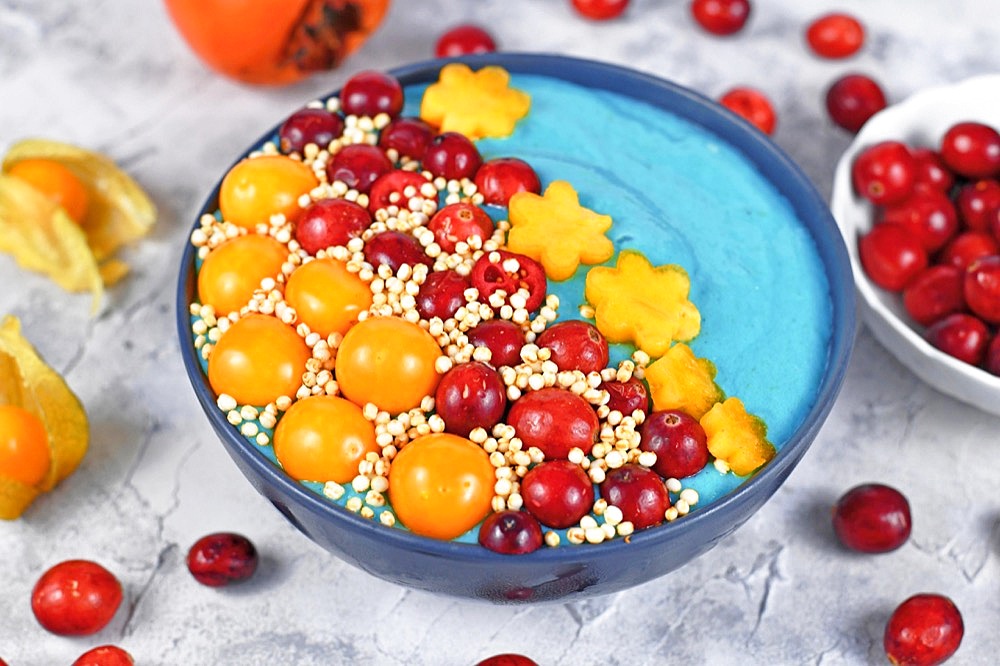 Healthy yogurt and fruit smoothie bowl with natural green spirulina powder and decorated with cranberries, physalis and kaki fruits and puffed quinoa grains