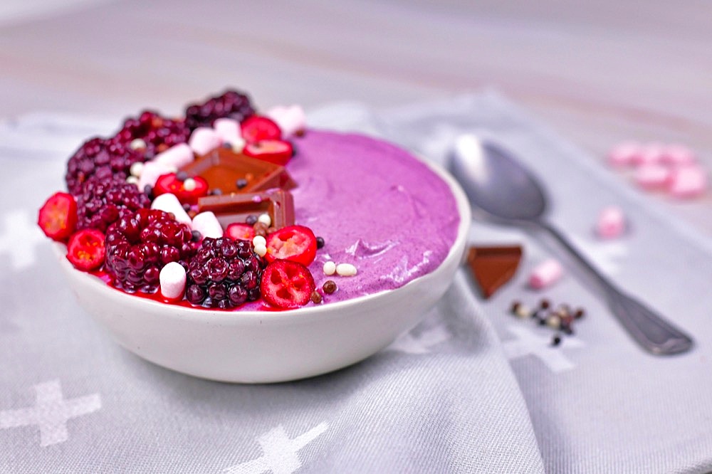 Fruit smoothie bowl decorated with healthy red raspberry, cranberry, small marshmallows and chocolate pieces