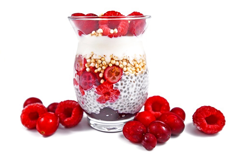 Healthy breakfast layered in glass with chia seed pudding, puffed quinoa grains and joghurt topped with red raspberry and cranberry fruits