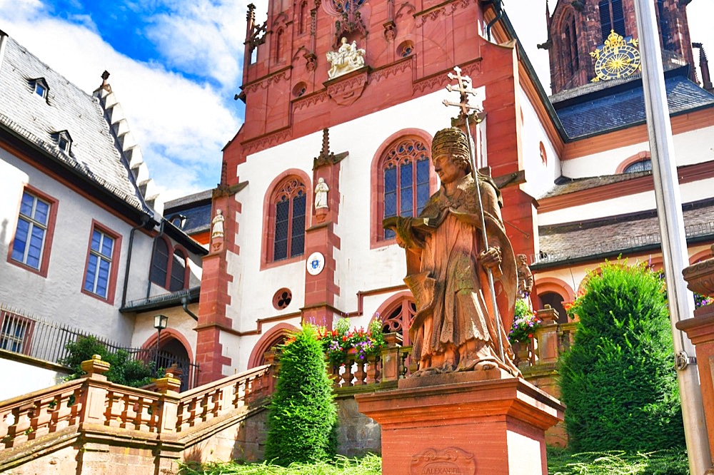 Aschaffenburg, Germany, July 2020: Statue of theologian Adolph Franz in front of historic Catholic curch called Kollegiatsstift St. Peter und Alexander or Stiftskirche, Europe