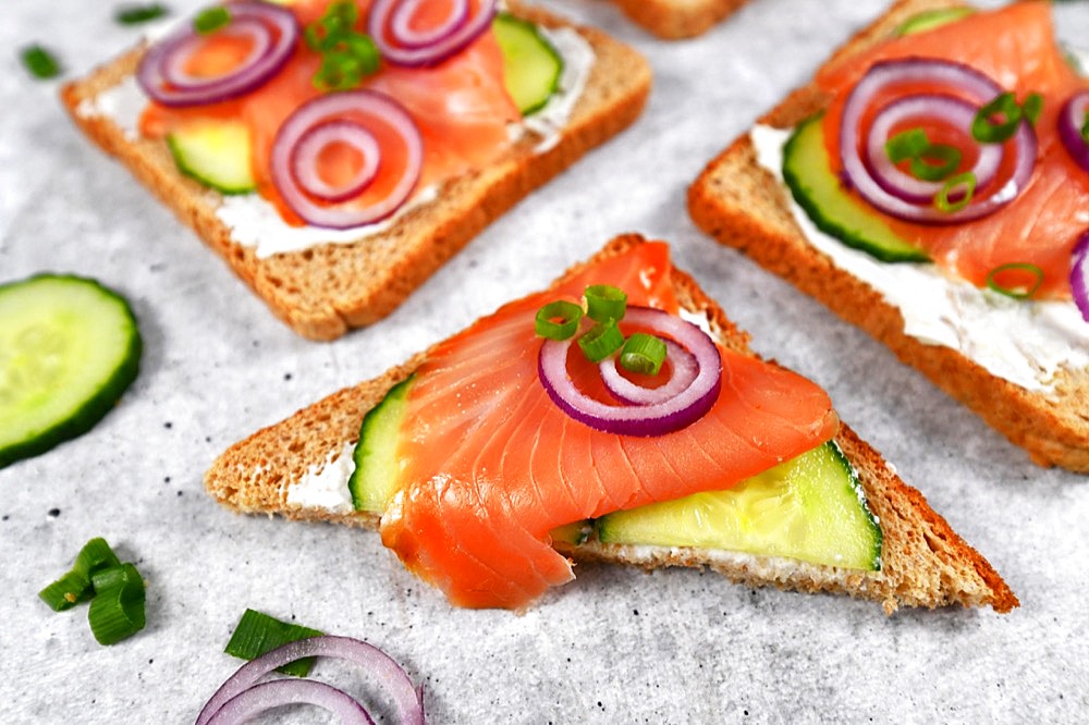 Half slice of healthy wholegrain toast bread topped with smoked salmon fish, red onions and spring onions and cucumber on horseradish