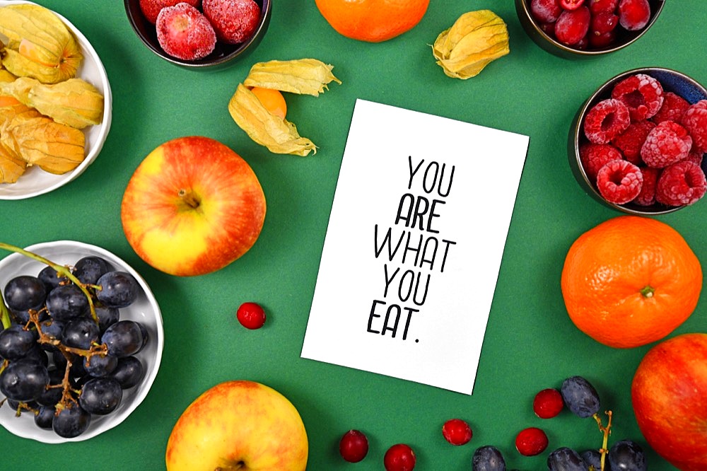 Healthy eating concept with You are what you eat card on green background surrounded by fruits like apples, grapes, berries and oranges