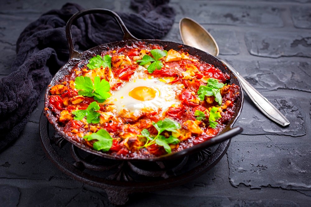 Shakshuka - dish of eggs poached in a tomato sauce with Feta cheese and coriander in baking pan