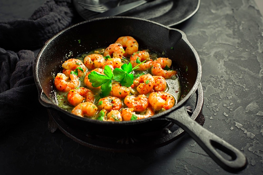 Shrimps with garlic, olive oil and parsley in frypan on black background