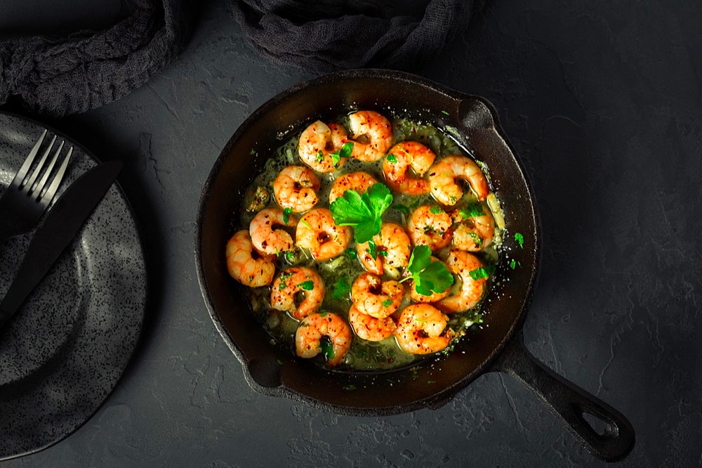 Shrimps with garlic, olive oil and parsley in frypan on black background