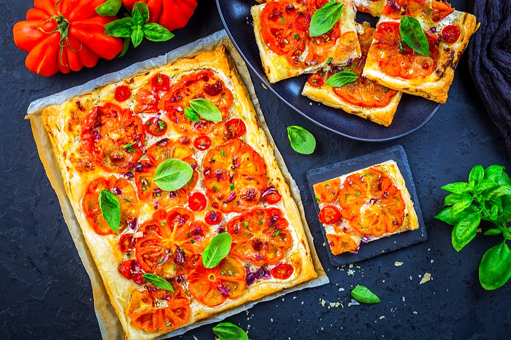 Vegetarian tomato tart or puffed pizza with herbs on black background