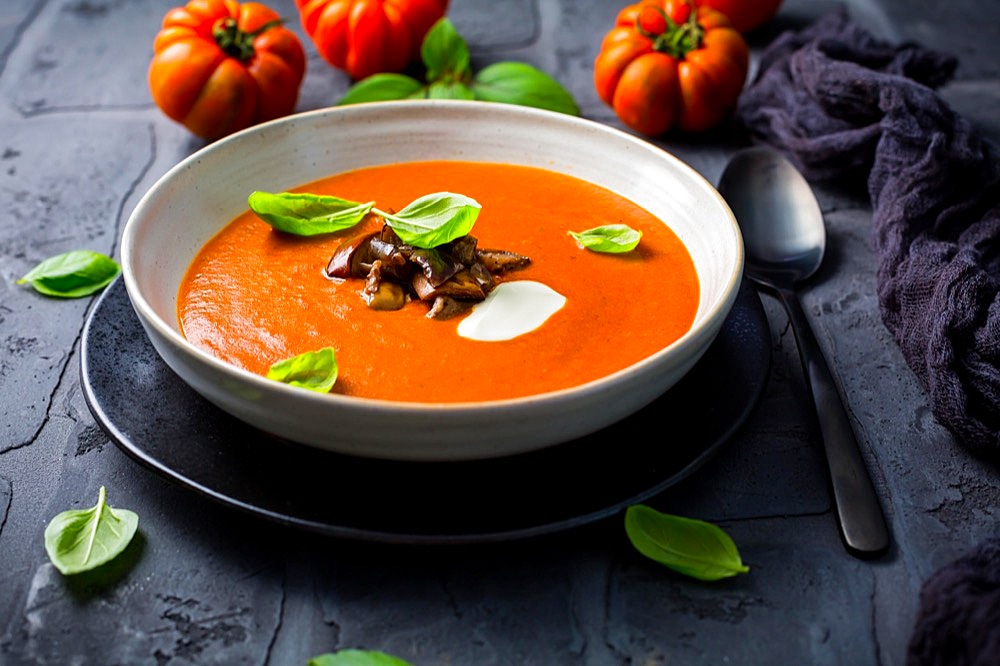 Homemade tomato soup with roasted eggplant and basil on dark background