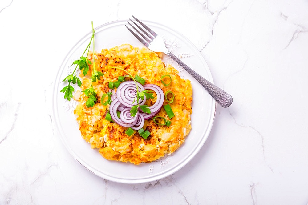 Tortilla - spanish omelet with potatoes, onions and herbs on white background