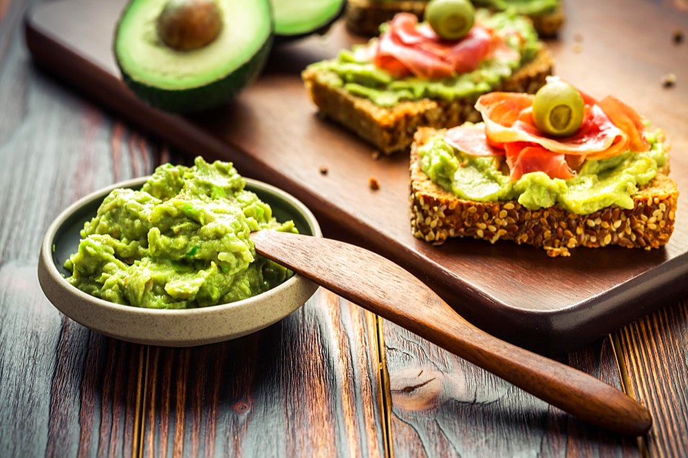 Guacamole dip or spread with open sandwiches and ham on wooden kitchen table