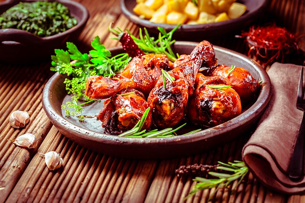 Marinated chicken drumsticks with baked potatoes and spinach on wooden background