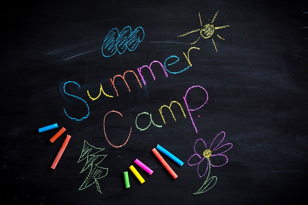 Text Summer camp written on black chalkboard, with chalk sticks of different colors