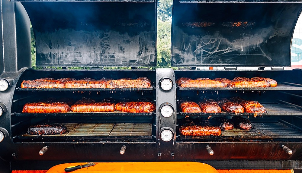 Large barbecue smoker grill with grilled meat wrapped with bacon. Street food