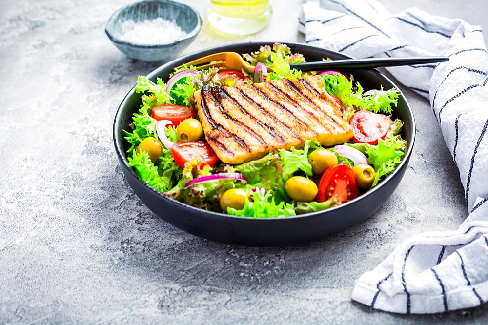 Fresh salad with grilled cheese, tomatoes and olives on grey