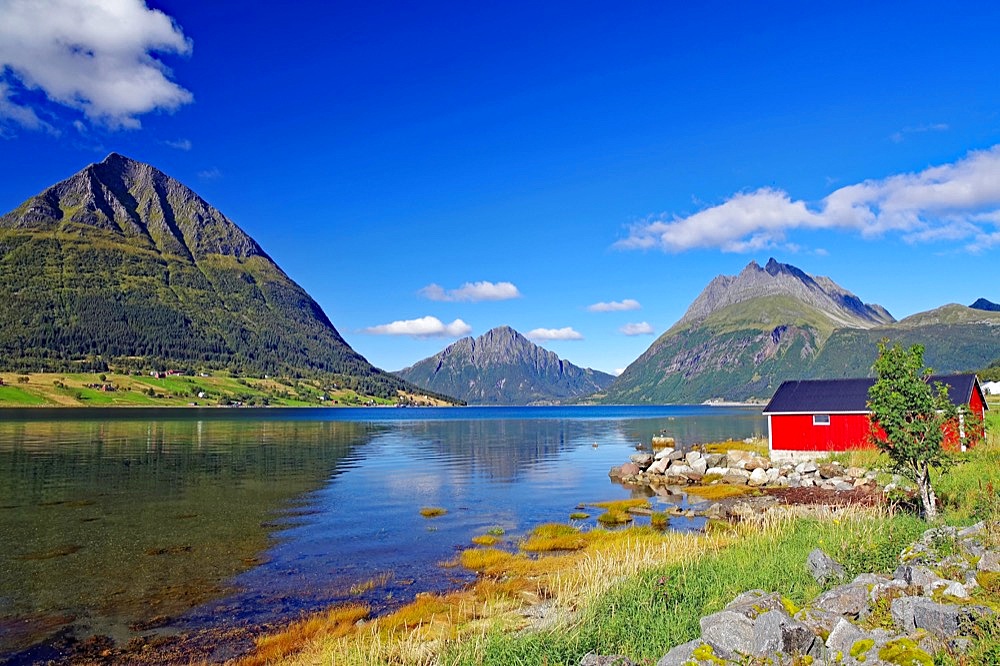 Red wooden house and high, rugged mountains by a fjord, shallow bay, Aldersund, FV 17, Kystriksveien, Nordland, Norway, Europe