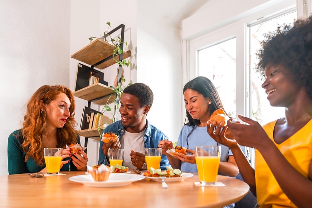 Friends at a breakfast with orange juice and muffins at home, relaxing in with domestic food and drink