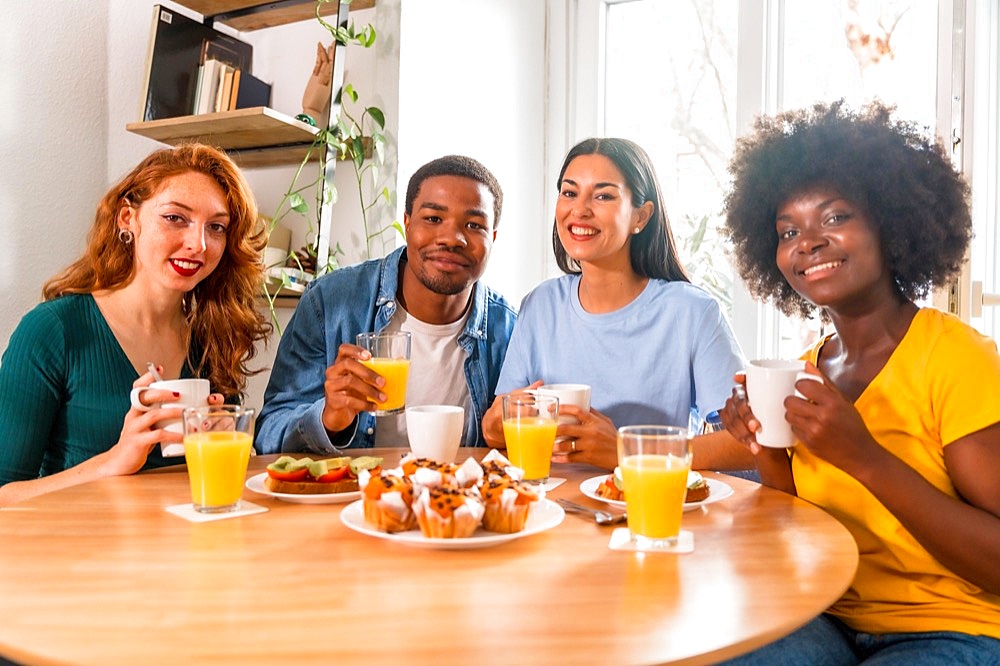 Multiethnic friends having breakfast with orange juice and muffins at home