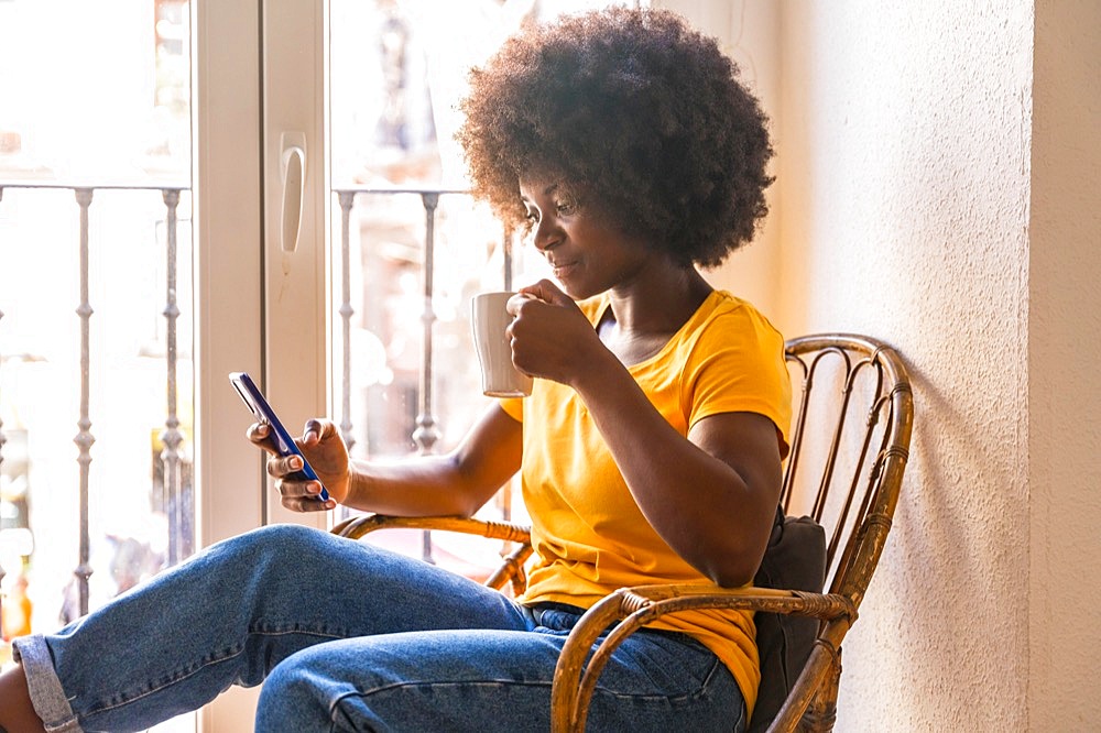 Afro hair woman by the window home having a hot drink, coffee in the morning