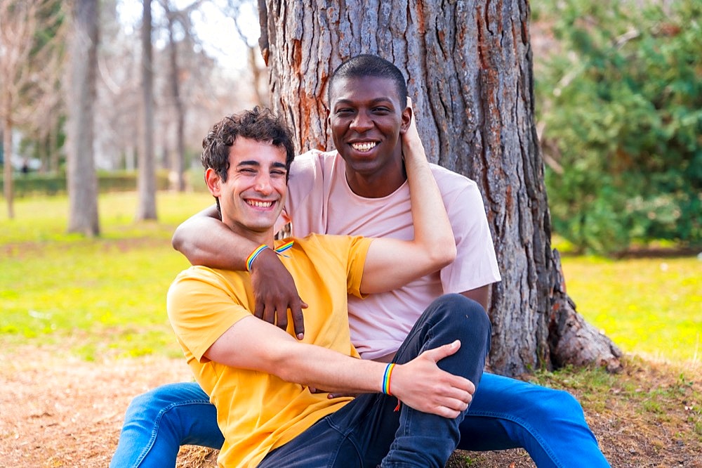 Couple of multi-ethnic men in a park, lgbt concept, sitting together a tree in a romantic pose