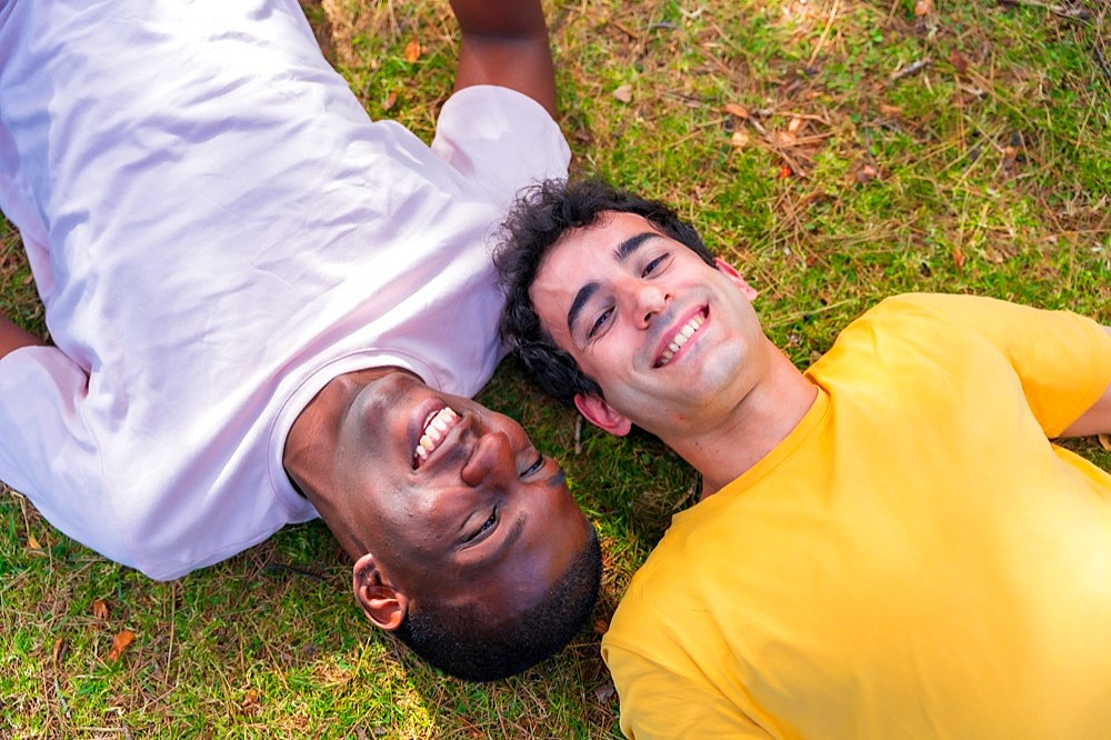 Couple of multi-ethnic men in a park, lgbt concept, lying on the grass