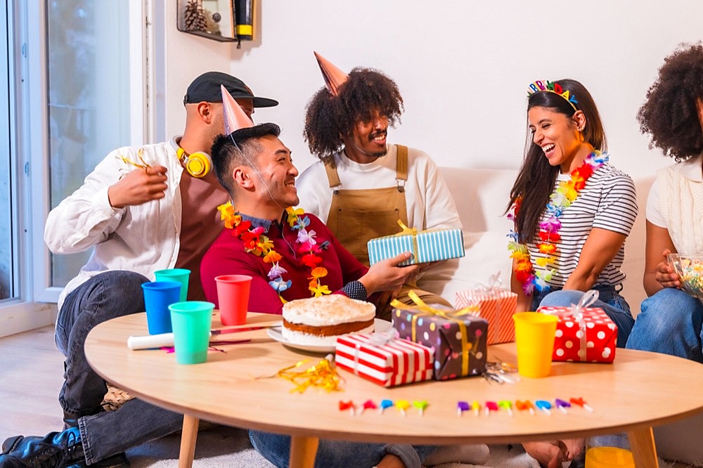 Group of friends at a birthday party on the sofa at home smiling delivering gifts