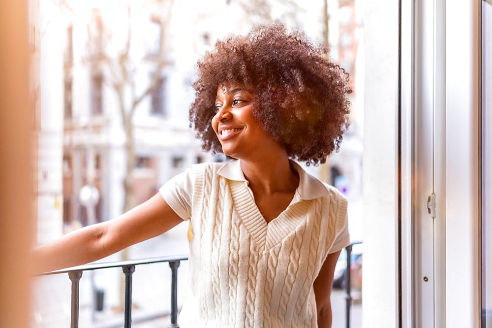 Portrait of a young black ethnic woman with afro hair on a balcony at home smiling, everyday situation, at sunset