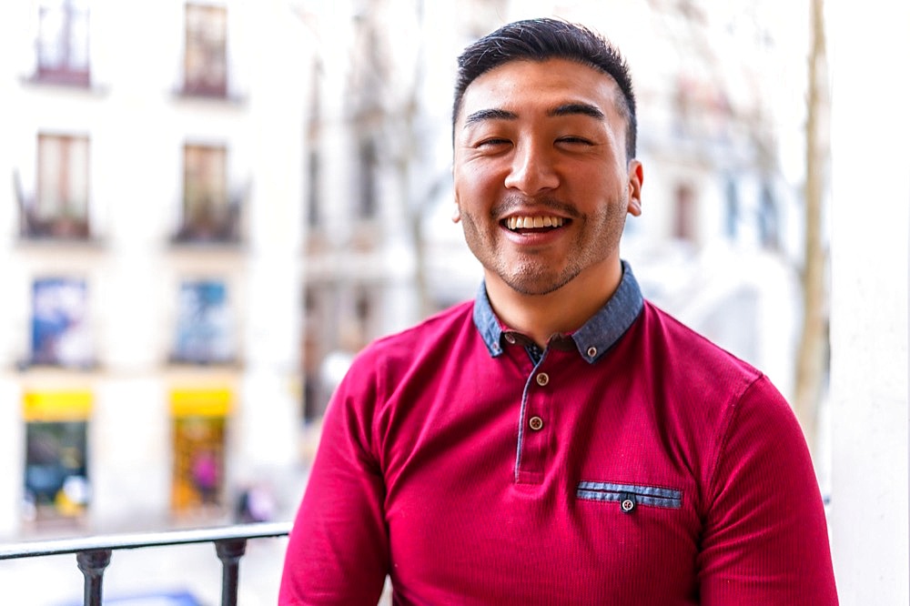 Portrait of a young Chinese man on a balcony at home smiling, everyday situation, apartment