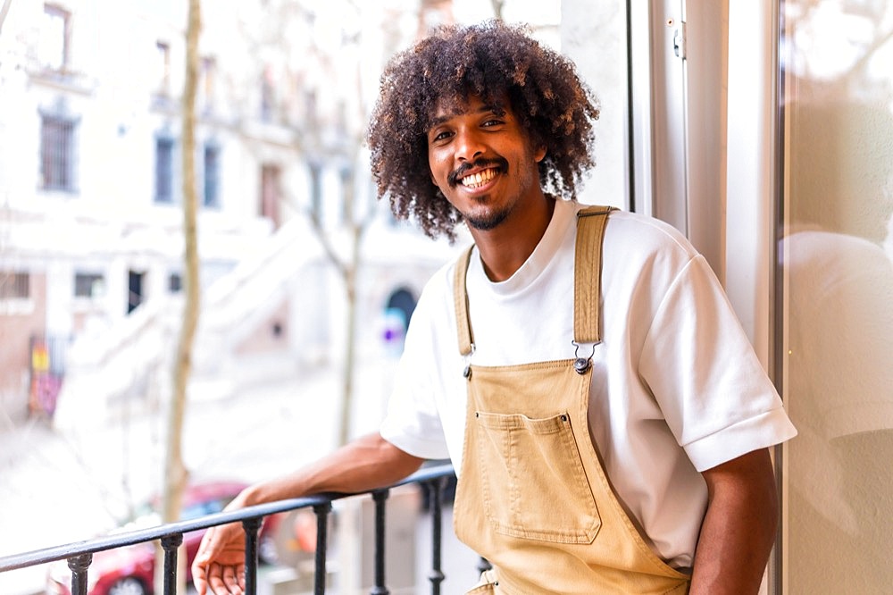 Portrait of a young black ethnic man on a balcony at home, everyday situation, apartment, smiling