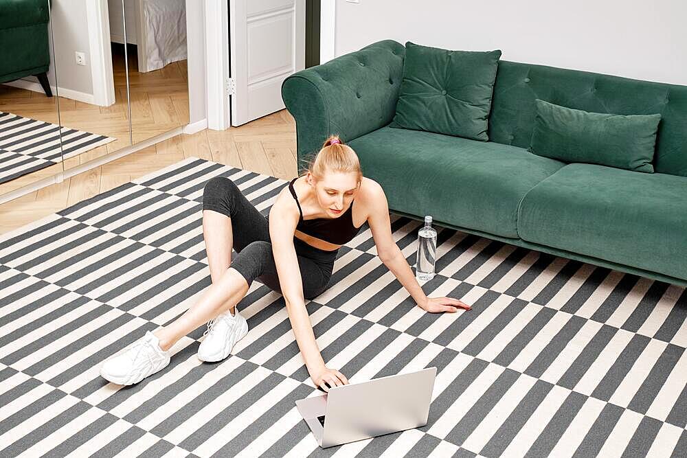 Young woman sits on the floor of her apartment and turn on video record with exercises