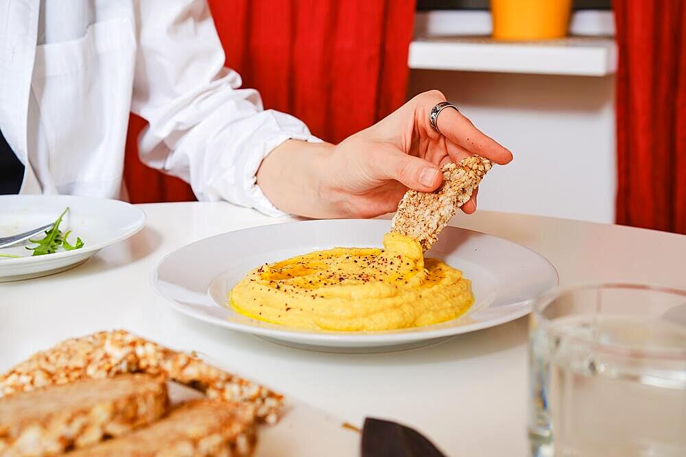 Female hand dipping piece of crispbread into bowl with hummus